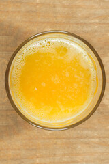 Overhead view of a glass full of squeezed orange juice on a wooden table. Healthy drinks, fruits, and juices.