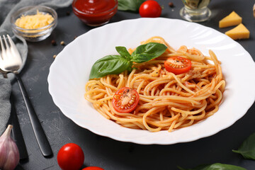 Spaghetti with tomato sauce and cherry tomatoes with basil on white plate on dark background