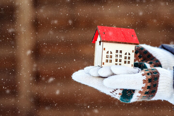 Small house in hand over winter background. Preparing the house for winter time.