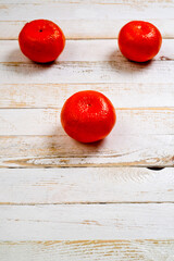 Three tangerines ripe and bright orange lying on a white wooden surface.