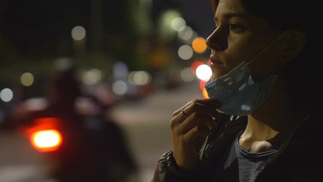 coronavirus - woman on the street at night pulls down her mask to breathe
