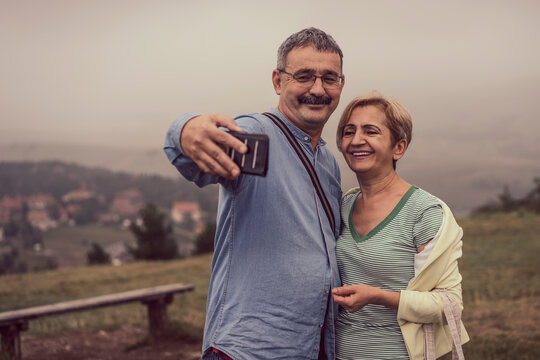 Beautiful older couple on mountain top surrounded with fog taking selfie pictures with phone