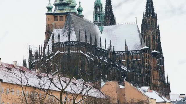 Gothic medieval castle in Europe. The roof is covered with snow, the copper spiers of the towers, the silhouette of bare branches of the trees against the gray sky. 