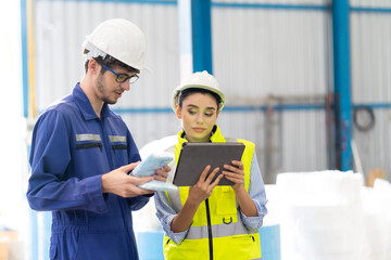 Female Inventory Manager checking stock on Digital Tablet. Man warehouse worker with hard hat safety helmet at storage buildings