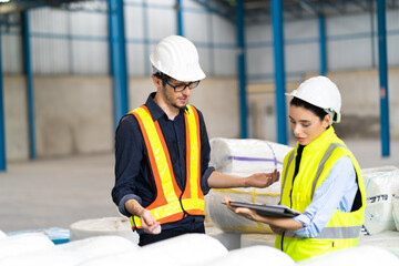 Female Inventory Manager checking stock on Digital Tablet. Man warehouse worker with hard hat safety helmet at storage buildings