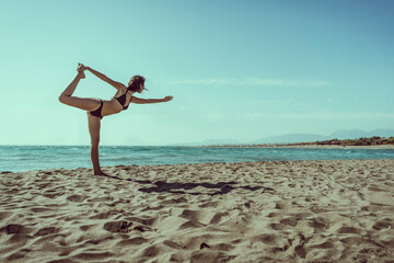 Beautiful young female doing yoga on beach. Gorgeous woman in bikini meditating on beach at summertime on vacation