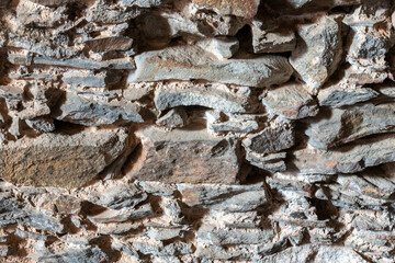 Ancient stone wall of the castle basement. Wall texture of ancient old brick stone. Outdoor exterior castle facade with destroyed uneven pattern of shabby rock. Solid wall sandstone structure