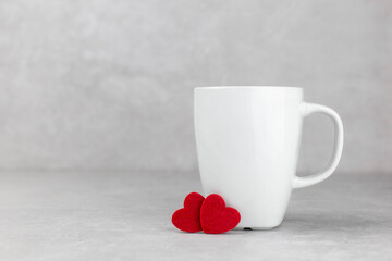 Blank white mug mockup with red hearts, light concrete stone background. Valentines, mothers, womens day composition. Side view. Copy space.