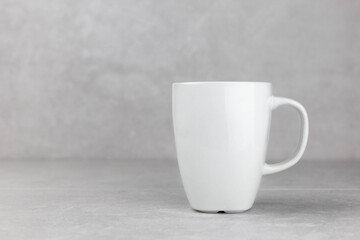 Classic white mug on light concrete stone background, blank template mockup style. Empty cup or drink mug. Side view. Copy space.