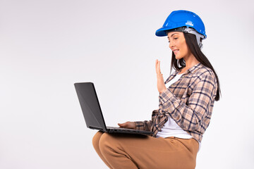 New norms and online concept. Woman in hard hat greeted by video communication while holding laptop on her feet. White background.