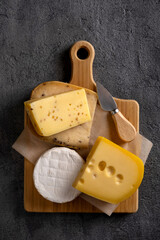 Various types of cheese on wooden board. Free space for your text. Dark moody. Top view.