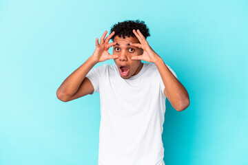 Fototapeta premium Young african american curly man isolated on blue keeping eyes opened to find a success opportunity.