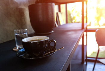 cup of coffee on table in coffee shop on black wood table near window with light shade on tabletop at cafe.