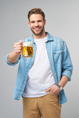 Young Man holding wearing jeans shirt holding glass of beer standing over Grey Background