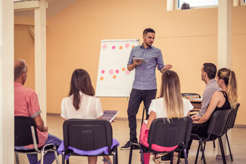 Group of people listening to a presentation. Man holding tablet and handling the workshop like a pro while speaking on seminar for professional development and team building