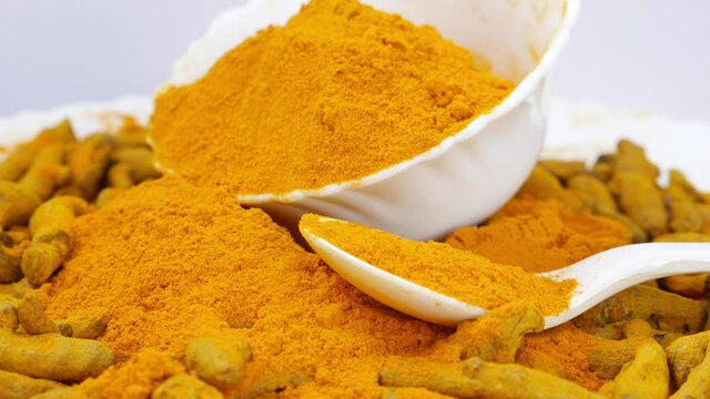 Close rotating shot plastic bowl filled with turmeric powder and a spoon filled with turmeric powder around