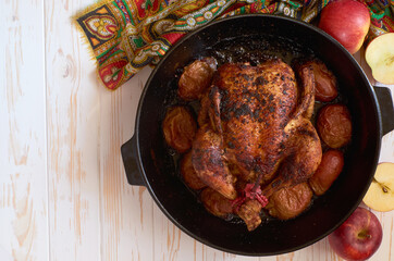 Oven roasted backed chiken with apples in cast iron skillet pan decorated with colorful napkin on the white wooden background food photo table top, flat lay view. For banner, advertising, copy spase.