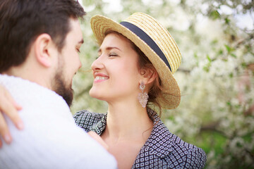 Fototapeta premium Young beautiful girl in a straw hat hugs her lover in a blooming spring garden