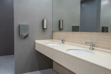 Bathroom with white washbasin and taps. Public restroom interior. Large mirror, dry towels,...