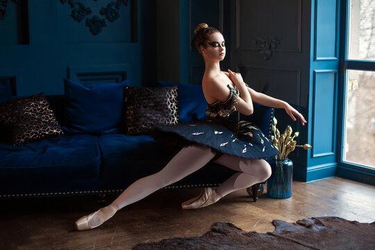 Ballerina in a dark blue ballet tutu sits on a sofa in a blue interior