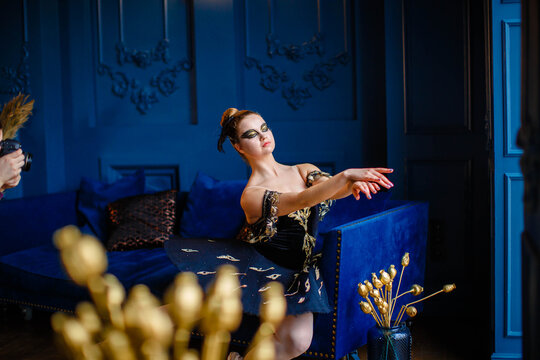Ballerina in a dark blue ballet tutu sits on a sofa in a blue interior