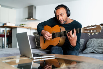 Obraz premium Relaxed man playing the guitar at home and using a laptop