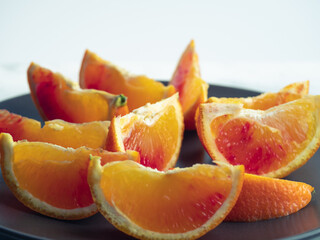 Fototapeta na wymiar Colorful fruit background. slices of red orange are on dark dish on bright background. Fresh citrus fruit rich of vitamins, juicy fruit, healthy nutrition. Orange color
