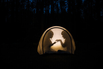 Children making shadow puppets in a camping tent at night