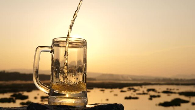 Drinks with a beautiful sunset,Beer is pouring into glass against natural background during sunset.
