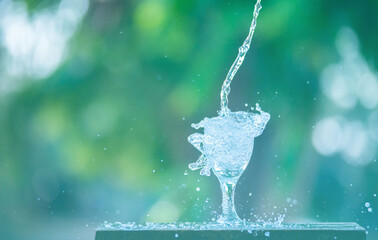 Water splash in glass Select focus blurred background.Drink water pouring in to glass over sunlight and natural green background.Nature conservation concept.