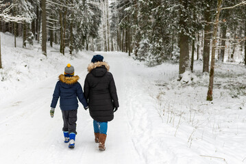 Fototapeta na wymiar Mother and son walking together on a forest track in winter time.