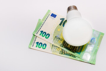 One LED bulb and 100 euro bills on white background