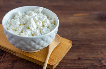 Homemade cottage cheese in a white bowl on a wooden background.
