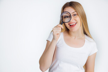 Funny joyful girl with beautiful long blond hair in a white t-shirt looking through a magnifying glass