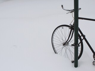 Black bicycle in Montreal, Canada, parked by a street sign in deep snow after a snowfall and a blizzard, cycling as popular means of city transportation in winter.