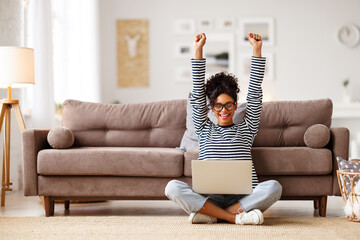 Glad woman celebrating good news while working on laptop at home - 407238386