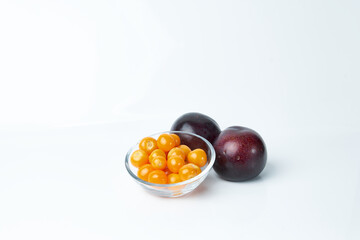 Glass container carrying cape gooseberries and next to it two juicy plums. Tropical fruits.