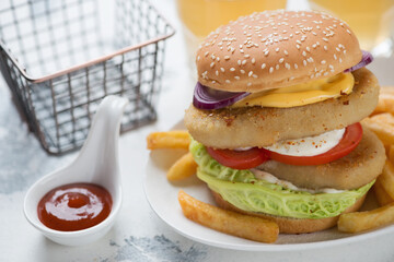 Close-up of double burger with sesame bun, fish cutlets, vegetables and french fries, studio shot on a white concrete background