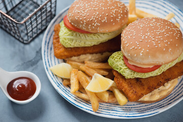 Blue and white plate with two fishburgers and french fries, studio shot on a grey concrete surface