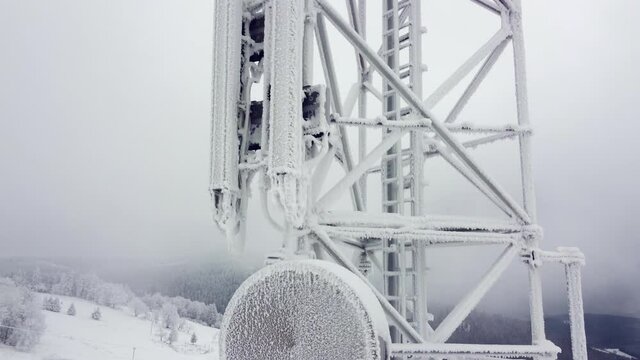 Drone shot, frosted telecom tower in mountain scenery. Mobile phone and internet transmitters, cold winter, dangerously frozen.
