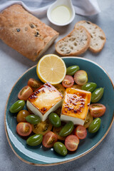 Turquoise plate with baked feta, tomatoes, green olives, ciabatta bread and olive oil, vertical shot
