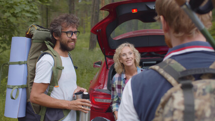 Group of friends or family standing together with camping gear near open car in forest