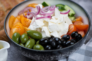 Grey bowl of greek salad with tomatoes, black and green olives, cucumber and chunks of feta cheese, studio shot, close-up