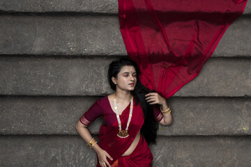 Portrait of beautiful Indian girl in heritage stepwell wearing traditional Indian red saree, gold...