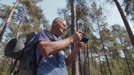 Senior man on hiking trip taking photos in forest with digital camera