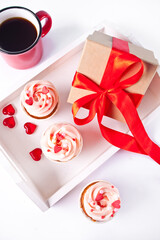 Valentines cupcakes cream cheese frosting decorated with heart candy, mug of coffee and gift box on the background.