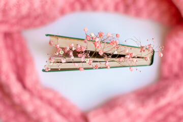 Green book with dry flowers on a pink warm knitted sweater background