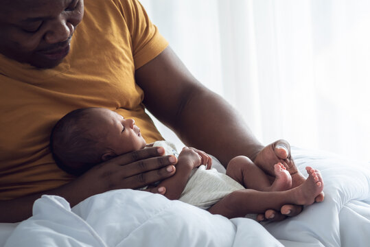 Blur soft images of An African American father holding  his 12-day-old baby newborn son lying in bed in a white bedroom,  concept to African American family and newborn