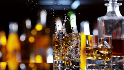 GLass of whisky with splashing liquid, bar on background