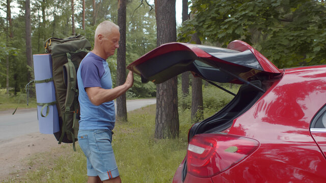 Senior Man Traveler Packing Camping Equipment Into Car Trunk Outdoors